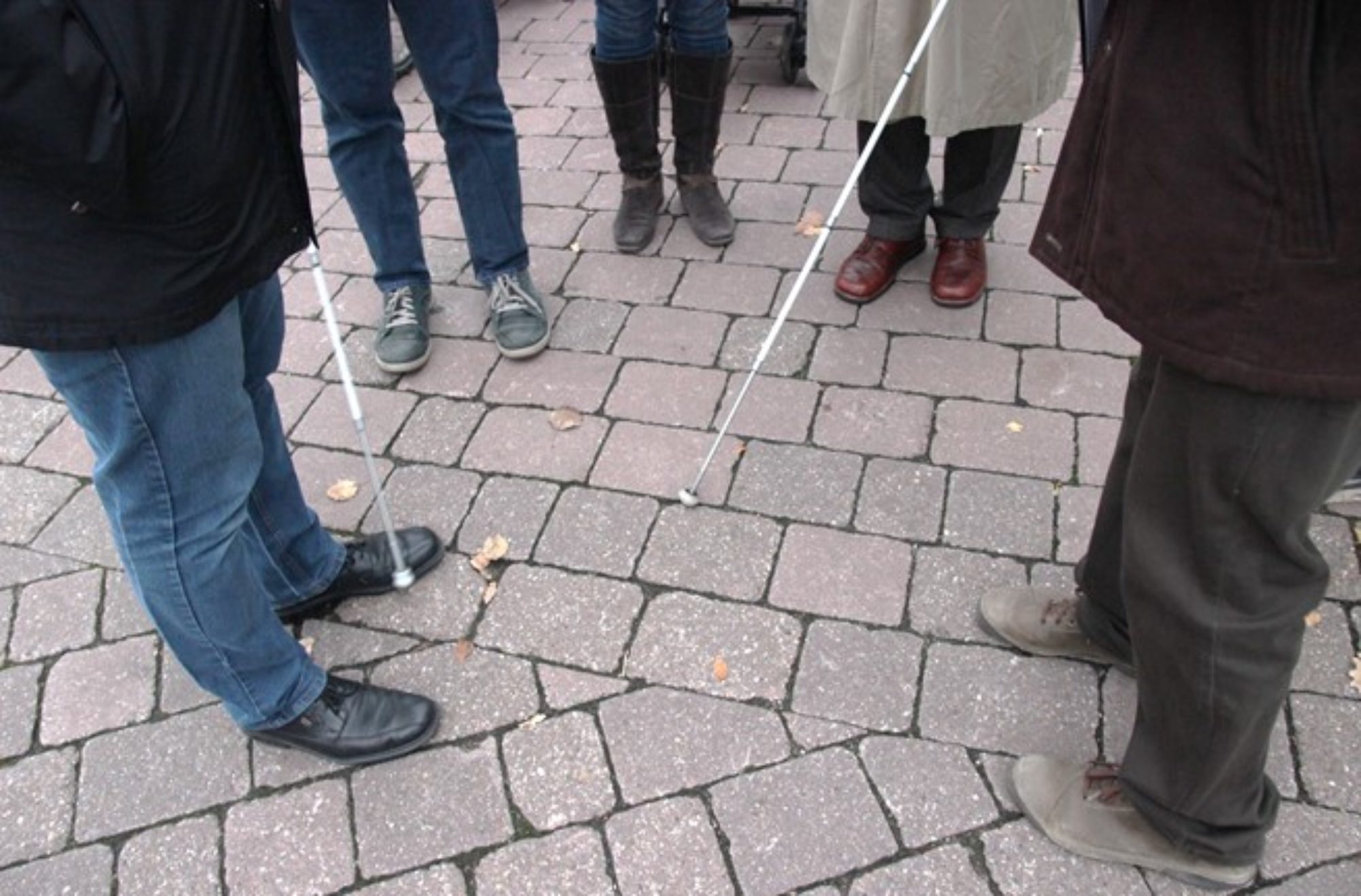 Das Foto zeigt Menschen, die im Halbkreis zusammenstehen. Zu sehen sind die Beine und zwei Blindenstöcke.